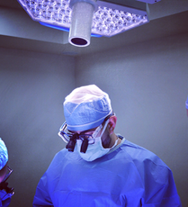 Surgeon in blue scrubs under operating room lights preparing for surgery.