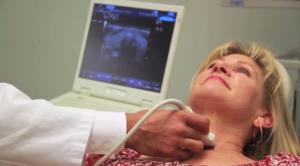 Woman undergoing a thyroid ultrasound with the monitor showing the scan in progress.