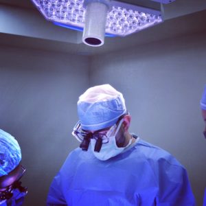 Surgeon in blue scrubs under operating room lights preparing for surgery.