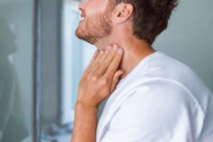 Man touching his throat in a gesture that suggests he's checking his neck or thyroid area.