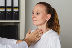 Doctor examining a patient's thyroid gland in a clinical setting.