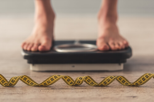 Person standing on a weight scale with a measuring tape in the foreground.