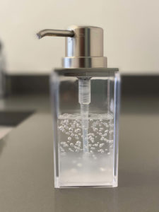 Transparent soap dispenser with a metallic pump on a counter.