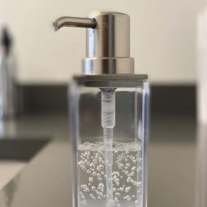 Transparent soap dispenser with a metallic pump on a counter.