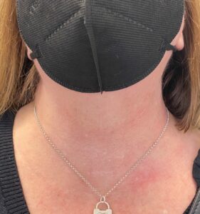 Person with a black face mask and a silver necklace with a pendant.